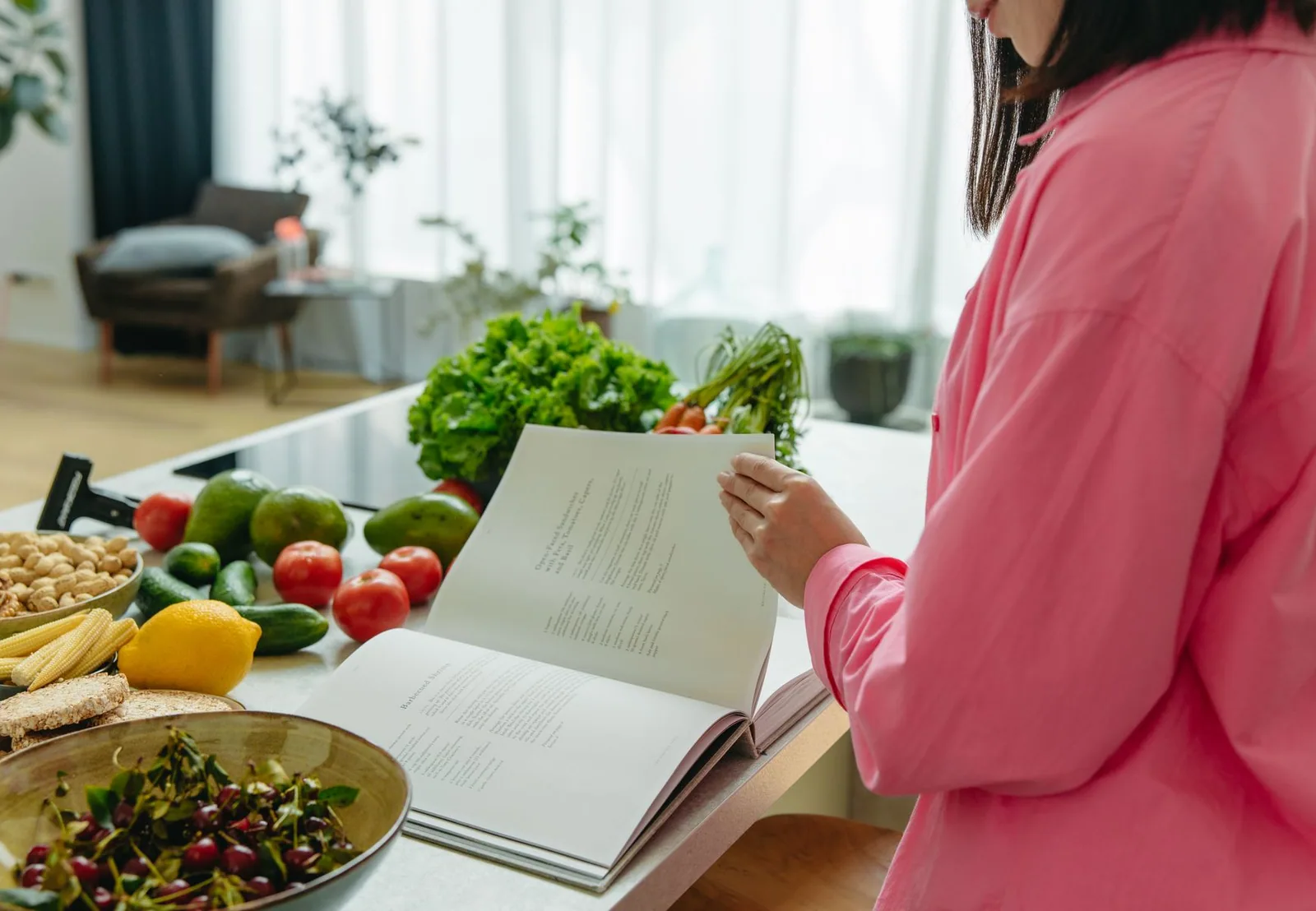 Mujer consultando un libro de cocina rodeada de verduras